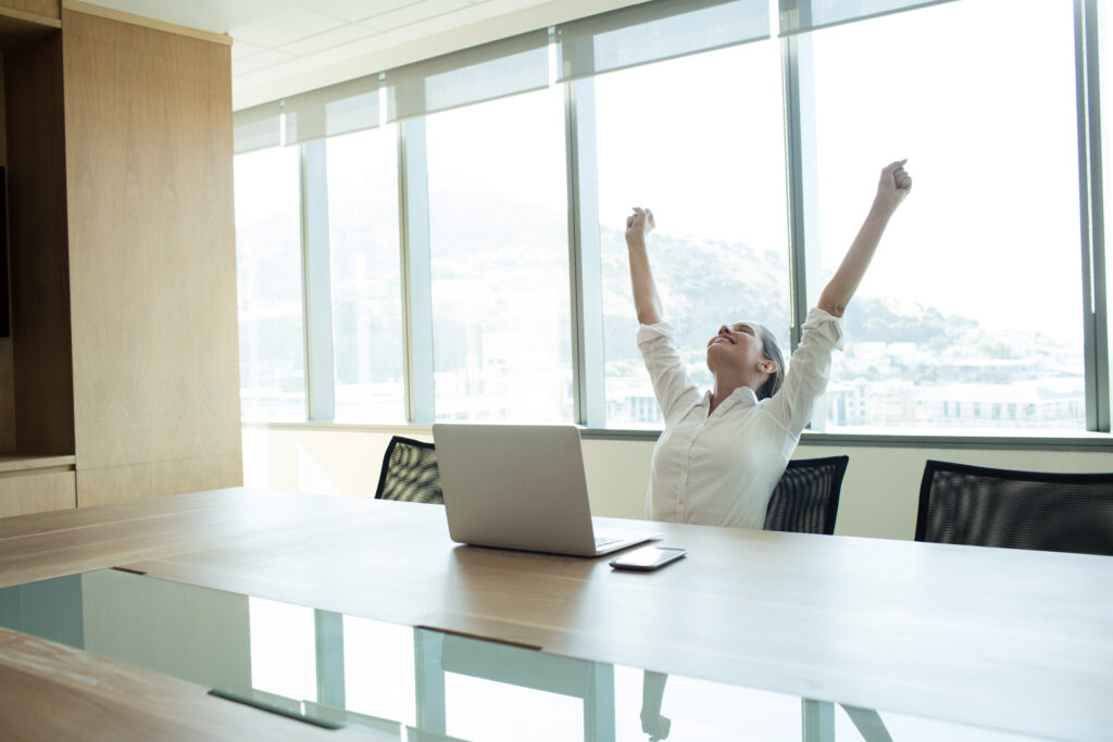 Cheerful businesswoman with arms raised sitting in conference room